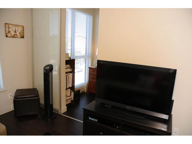 Living room with dark wood furniture, large window, and a flat-screen TV. - 306-215 East 33rd Ave, Vancouver East Side