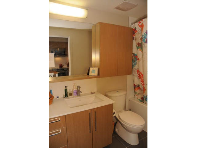 Furnished 1-bedroom bathroom with wooden cabinets and a floral shower curtain. - 306-215 East 33rd Ave, Vancouver East Side
