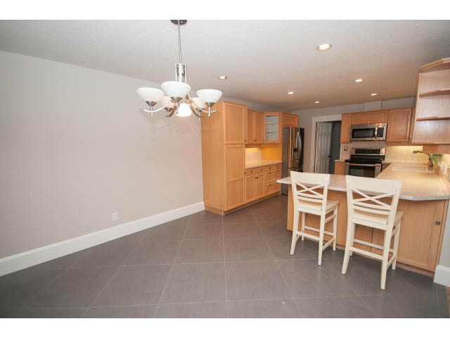 Bright kitchen with light wood cabinets and white countertops, open to dining area with white chairs. - 2704 Sechelt Drive, North Vancouver