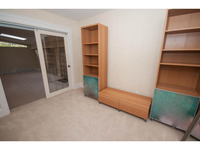 Bright living room with sliding glass door, light wood shelving, and neutral carpeting. - 2704 Sechelt Drive, North Vancouver