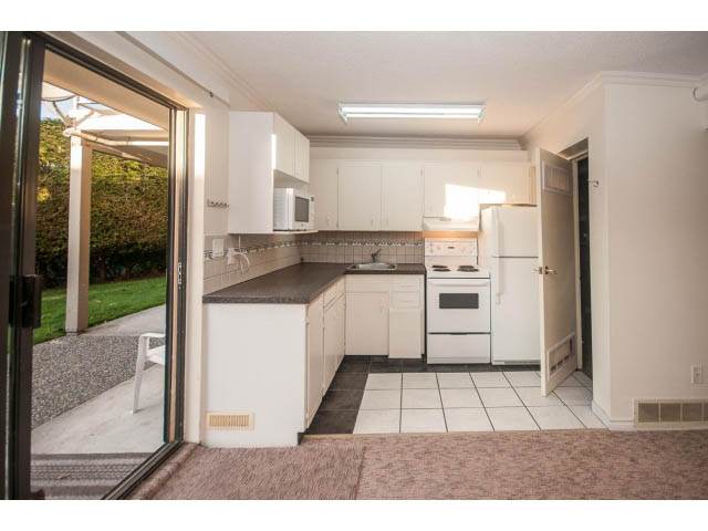 Bright kitchen with white cabinets, black countertops, and sliding glass door leading to a patio. - Suite- 3897 St. Pauls Ave, North Vancouver