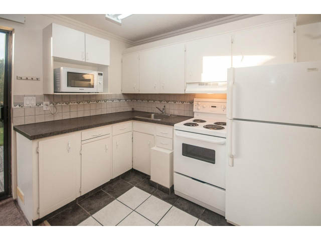 Bright kitchen with white cabinets, black countertops, and a small window above the sink. - Suite- 3897 St. Pauls Ave, North Vancouver