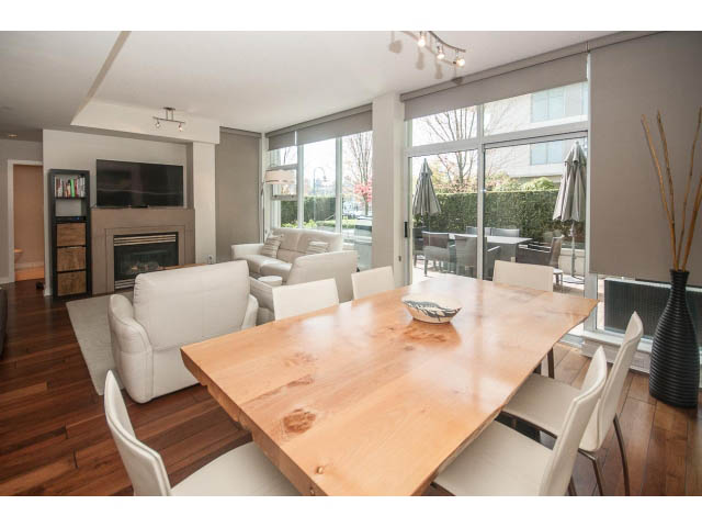Spacious dining room with wooden table, modern furniture, and large windows offering a view of greenery.