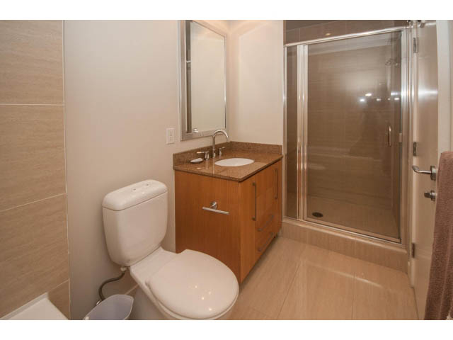 Bright bathroom with wooden cabinets, granite countertops, and a walk-in shower. - 106 - 633 Kinghorne Mews, Vancouver Downtown
