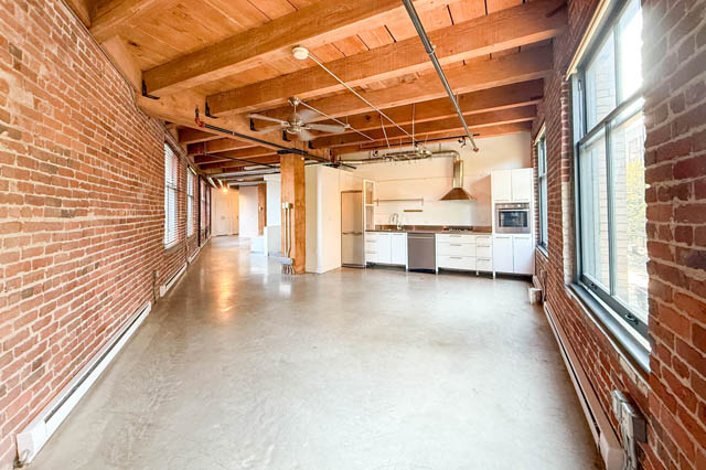 Spacious loft kitchen with white cabinets, stainless steel appliances, and exposed brick walls. - 221 - 55 E. Cordova, Vancouver Downtown