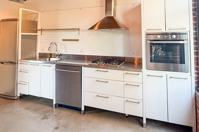 Modern kitchen with stainless steel countertops and white cabinetry, featuring a gas stove and built-in oven.