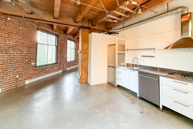 Open-concept loft kitchen with white cabinets, stainless steel appliances, and concrete floors. - 221 - 55 E. Cordova, Vancouver Downtown