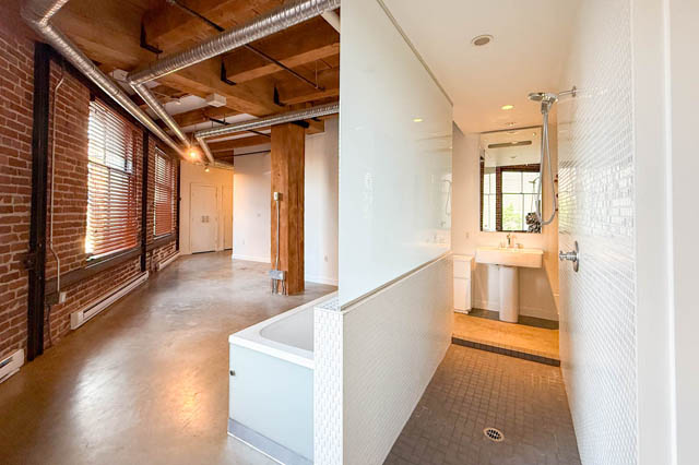 Spacious loft with exposed brick, concrete floors, and modern bathroom with mosaic tiles and a walk-in shower.