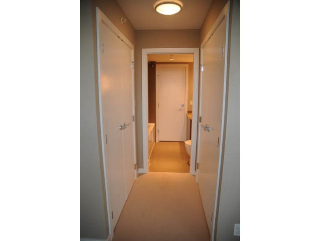 Furnished hallway with beige walls and carpeted floors leading to a door. - 310 - 135 East 17th Street, North Vancouver