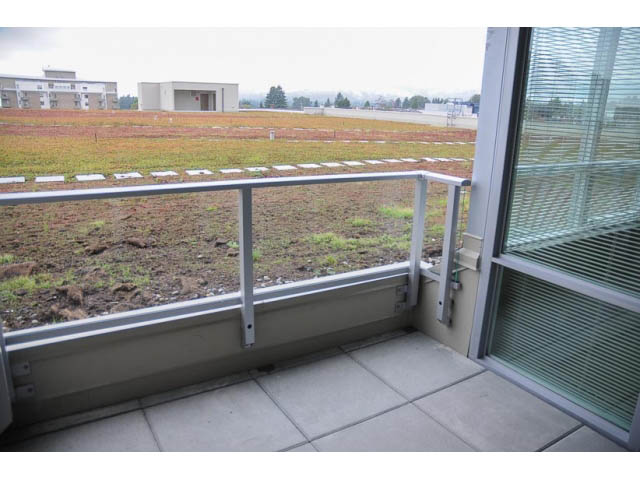 Balcony with view of open field and distant buildings, modern glass doors. - 310 - 135 East 17th Street, North Vancouver