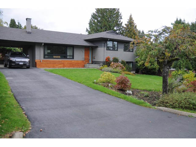 Bright living room with large windows and wooden accents, surrounded by lush greenery. - 1362 East 20th St, North Vancouver