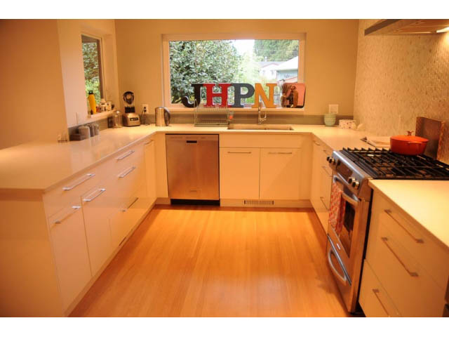 Bright kitchen with white countertops, hardwood floors, and a city view through the window. - 1362 East 20th St, North Vancouver