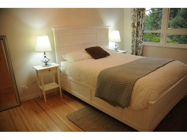 Spacious bedroom with hardwood floors and a large window, featuring a comfortable bed and bedside lamps. - 1362 East 20th St, North Vancouver