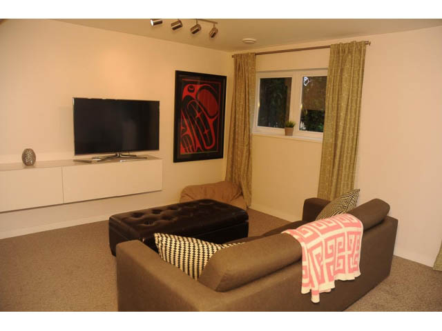 Furnished living room with modern furniture, a flat-screen TV, and a window with curtains. - 1362 East 20th St, North Vancouver