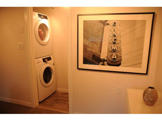 Laundry room with white appliances, hardwood floors, and framed movie theater sign art. - 1362 East 20th St, North Vancouver
