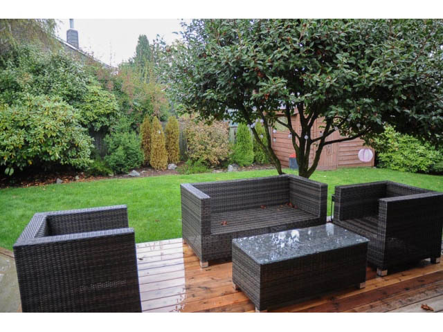 Furnished patio with wicker furniture and wooden deck, surrounded by greenery. - 1362 East 20th St, North Vancouver