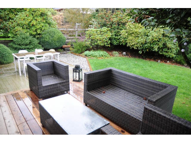 Furnished patio with wicker furniture and grassy area, surrounded by greenery. - 1362 East 20th St, North Vancouver