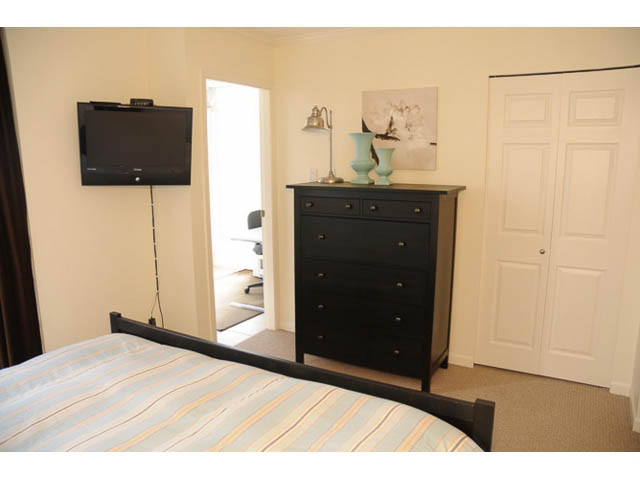 Furnished bedroom with a striped bedspread, black dresser, and wall-mounted TV. - 121 -1228 Marinaside Crescent, Vancouver Downtown