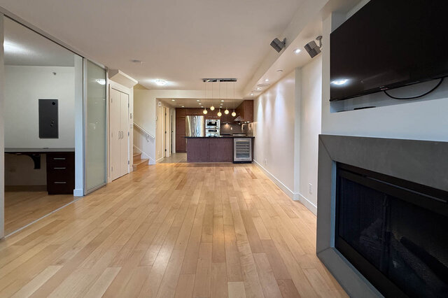 Open-concept living room with hardwood floors and a modern kitchen featuring stainless steel appliances and pendant lighting.
