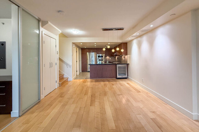 Open-concept living space with hardwood floors and a modern kitchen featuring stainless steel appliances and pendant...