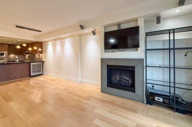 Open-concept living room with hardwood floors, modern fireplace, and kitchen counter. - 3238 Tupper Street, Vancouver West Side
