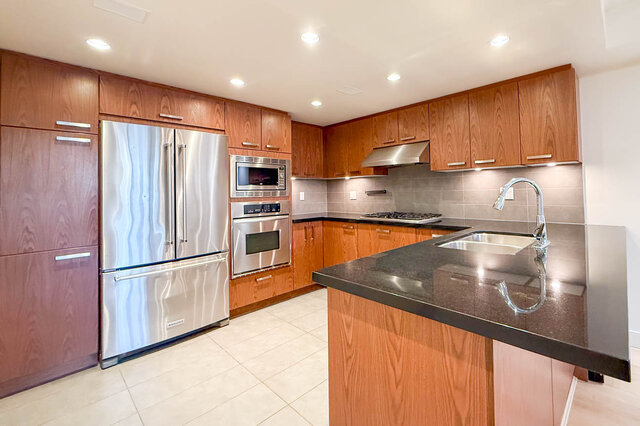Modern kitchen with granite countertops and stainless steel appliances, featuring a sleek island and ample cabinetry.