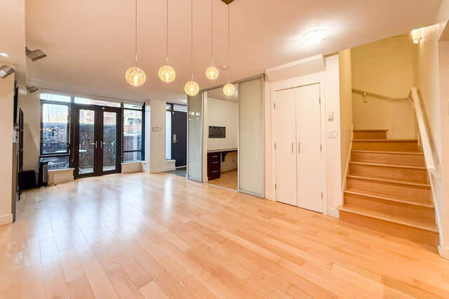 Spacious open-concept living room with hardwood floors, modern pendant lights, and a sliding glass door leading to a...
