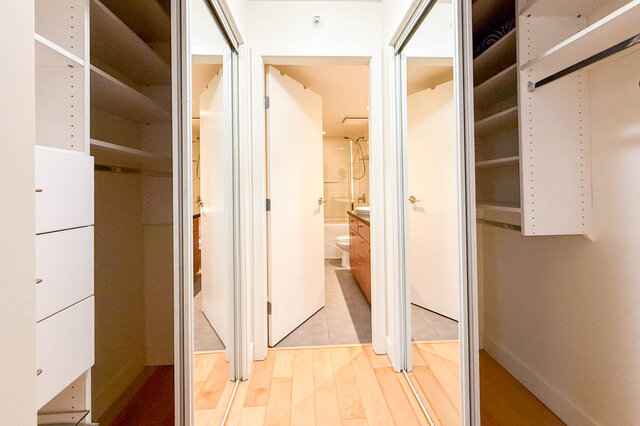 Spacious walk-in closet with sliding doors and built-in shelves, leading to a modern bathroom with a toilet and shower.