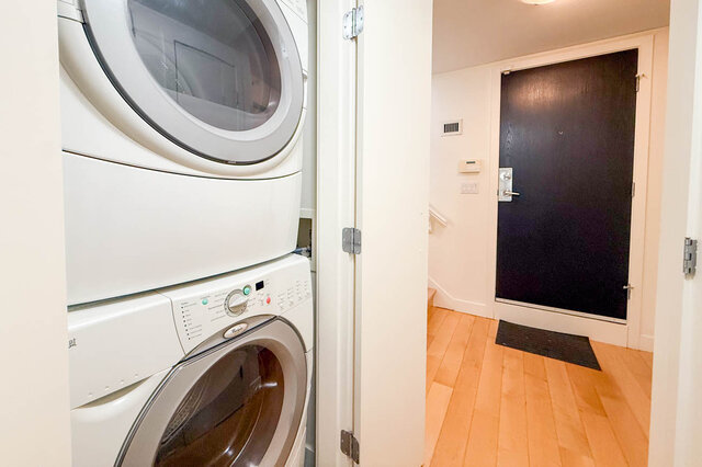 Laundry room with stacked washer and dryer, hardwood floors, and black door. - 3238 Tupper Street, Vancouver West Side