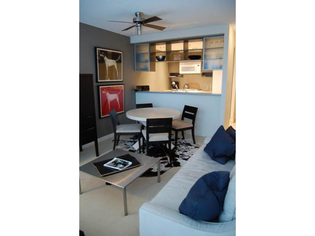 Bright kitchen with white cabinets and stainless steel appliances, open to a cozy living area with a white couch and dark...