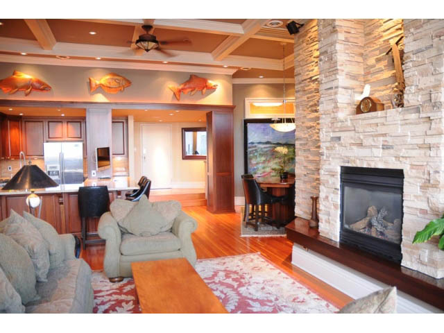 Furnished living room with stone fireplace, hardwood floors, and kitchen in background. - 654 Millbank, Vancouver West Side