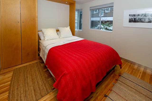 Furnished bedroom with hardwood floors and a red quilt, large windows letting in natural light. - 834 W 7th Ave, Vancouver West Side