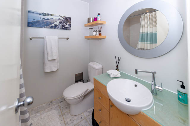 Furnished bathroom with modern sink, round mirror, and wooden shelves. - 834 W 7th Ave, Vancouver West Side