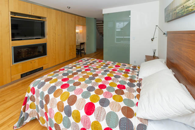 Spacious bedroom with hardwood floors, modern furniture, and a cozy fireplace. - 834 W 7th Ave, Vancouver West Side