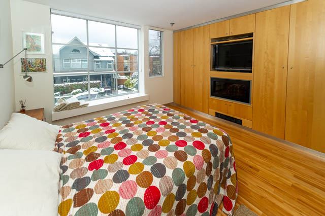 Furnished bedroom with hardwood floors, city view, and a colorful patterned bedspread. - 834 W 7th Ave, Vancouver West Side