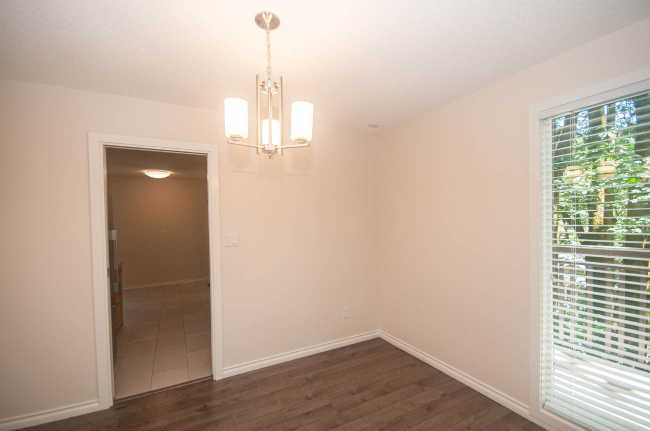 Spacious dining room with hardwood floors and a chandelier, leading to a cozy bedroom. - 1059 Heritage Blvd, North Vancouver