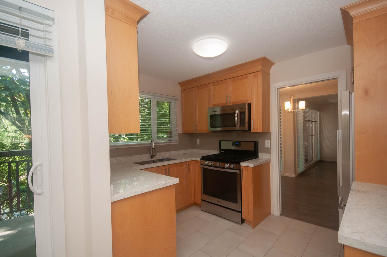 Bright kitchen with light wood cabinets, granite countertops, and a window view. - 1059 Heritage Blvd, North Vancouver