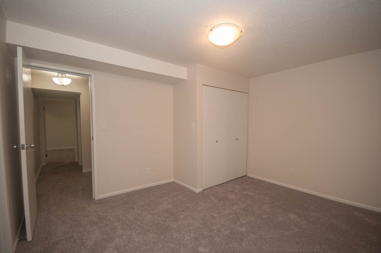 Spacious living room with carpeted floors and neutral walls, leading to a hallway. - 1059 Heritage Blvd, North Vancouver