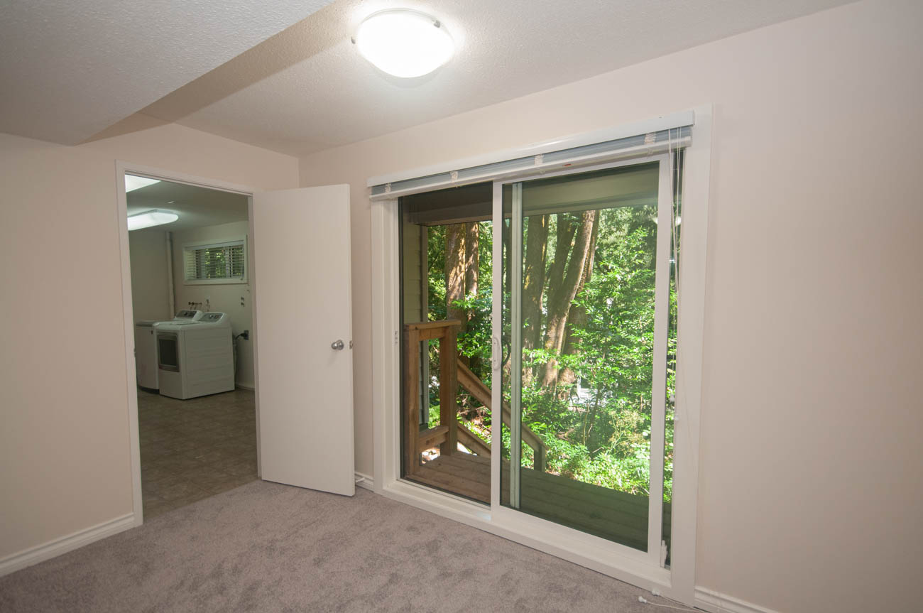 Spacious living room with sliding glass door to forest view, leading to laundry area. - 1059 Heritage Blvd, North Vancouver