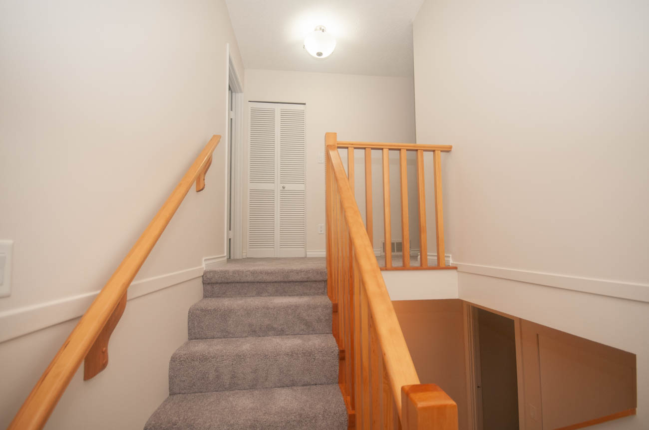 Staircase leading to upper level with wooden railings and carpeted steps. - 1059 Heritage Blvd, North Vancouver