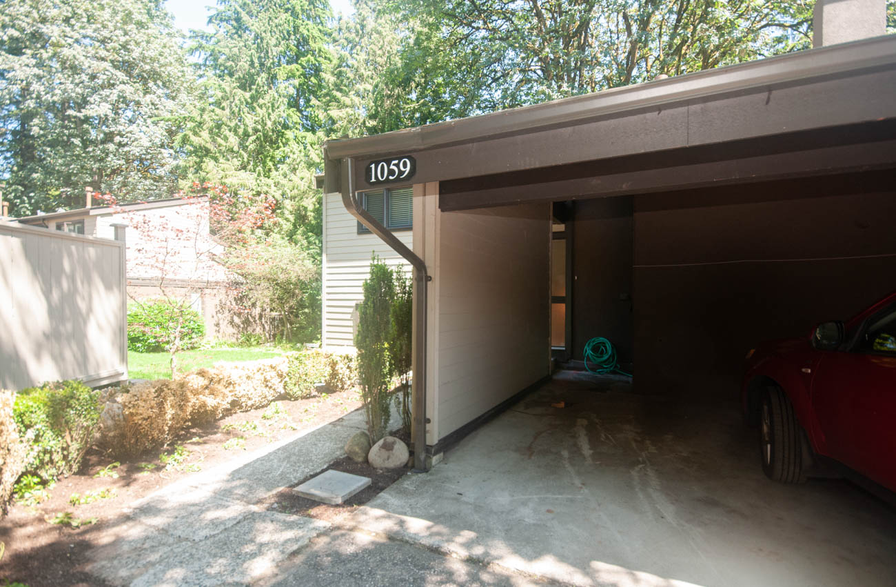 Open garage with red car and green hose, showcasing a cozy and functional space. - 1059 Heritage Blvd, North Vancouver