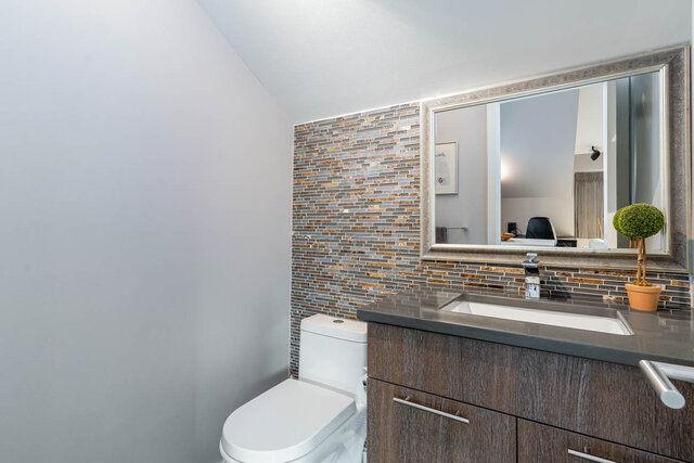 Modern bathroom with a sleek vanity, tiled backsplash, and a large mirror. - 420-B Tempe Crescent, North Vancouver