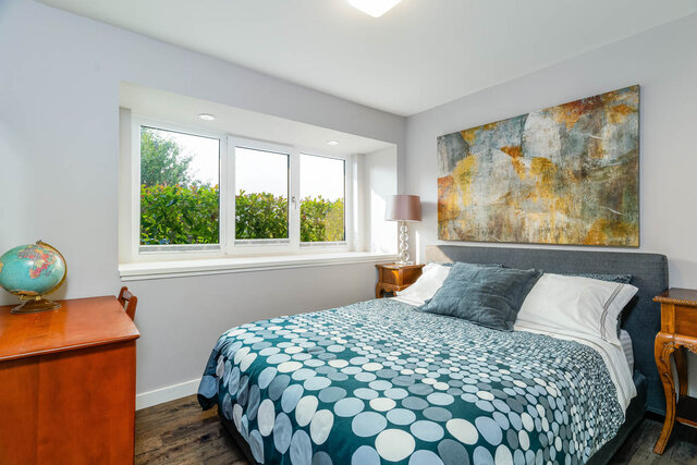 Spacious bedroom with twin beds, patterned bedding, hardwood floors, and a large abstract painting above the headboard.