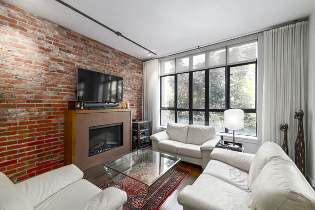 Spacious living room with exposed brick wall, large windows, and modern furnishings. - 302 - 1241 Homer Street, Vancouver Downtown