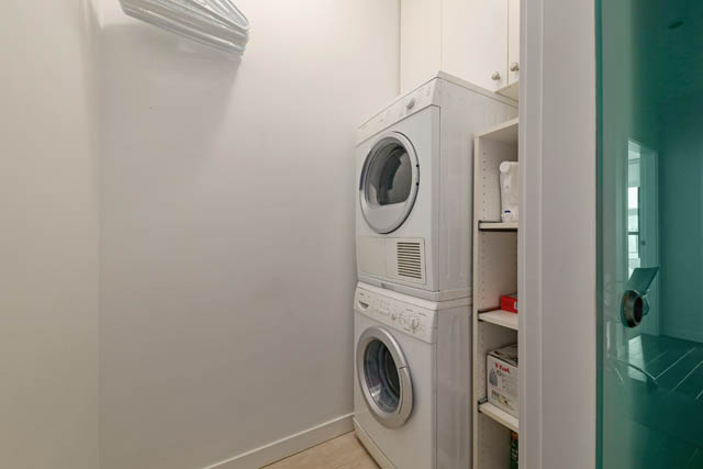 Laundry room with stacked washer and dryer, white cabinets, and teal accents. - 302 - 1241 Homer Street, Vancouver Downtown