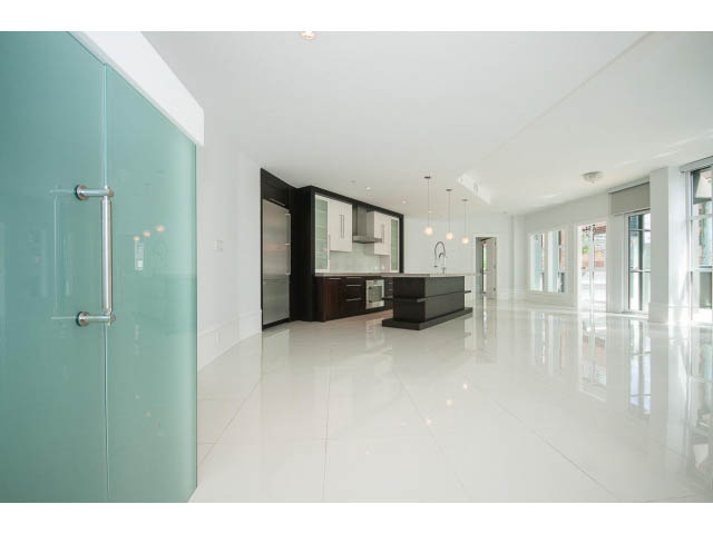 Bright kitchen with glossy white countertops and sleek black cabinetry, open to a modern living area.