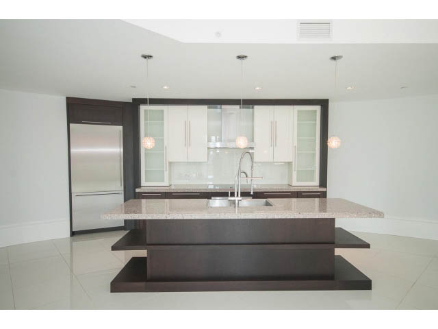 Bright kitchen with modern island, granite countertops, and stainless steel appliances.
