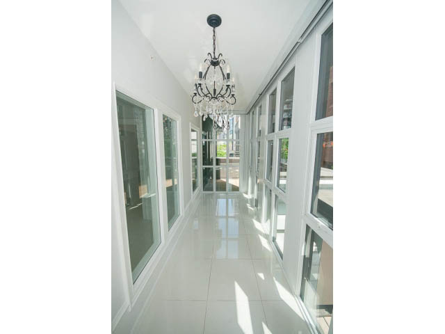 Bright hallway with large windows and elegant chandelier, leading to a sunlit living area.