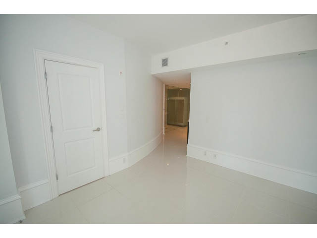 Bright living room with white walls, glossy tile floors, and a door leading to another room.