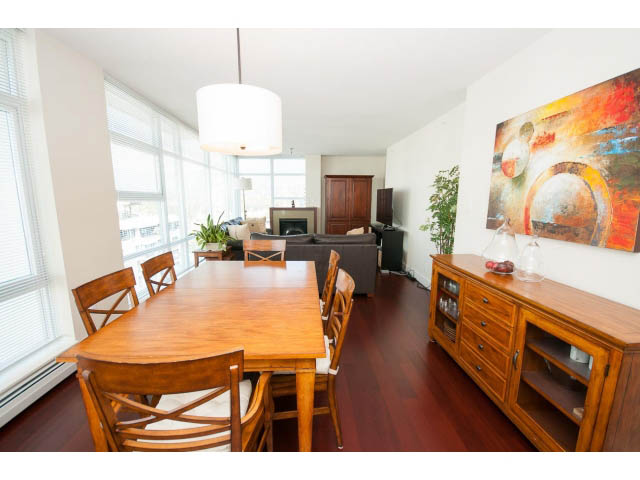 Furnished dining area with wooden table and chairs, hardwood floors, and a large abstract painting on the wall.